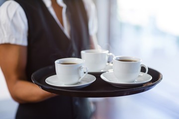 Mid section of waitress holding a tray of coffee cups