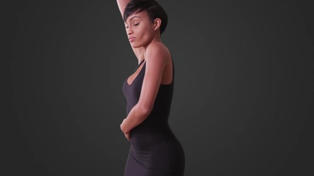 Sexy woman in tight black dress dancing on grey background. African American woman with short hair.