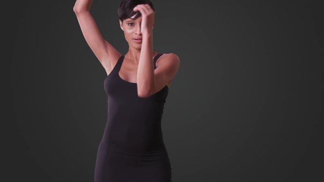 Sexy woman in tight black dress dancing on grey background. African American woman with pixie haircut.