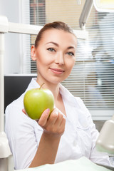 Portrait of beautiful female doctor in white uniform smiling and holding green fresh ripe apple. Face expressions, emotion, healthcare, medicine, occupation.