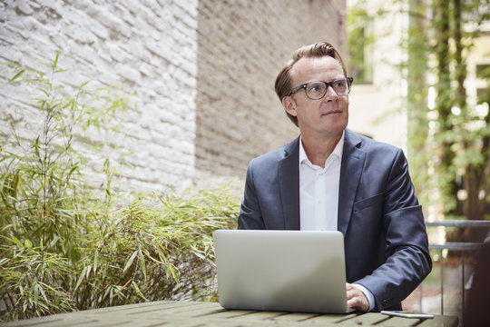 Businessman sitting with laptop at table in a backyard