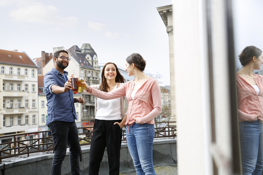 Man and two women clinking bottles on roof terrace
