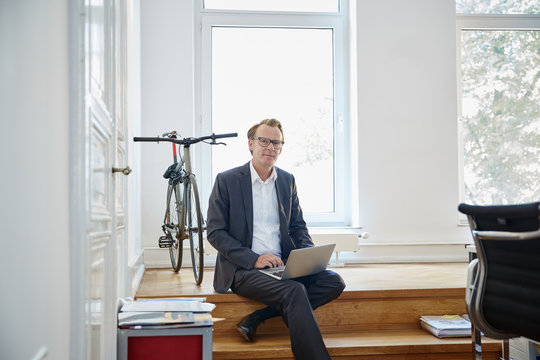 Businessman with laptop sitting on steps in an office
