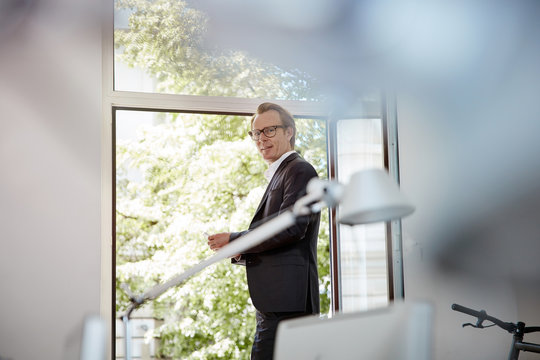 Smiling businessman standing in front of opened window