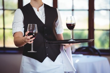 Mid section of waitress offering a glass of red wine in restaurant