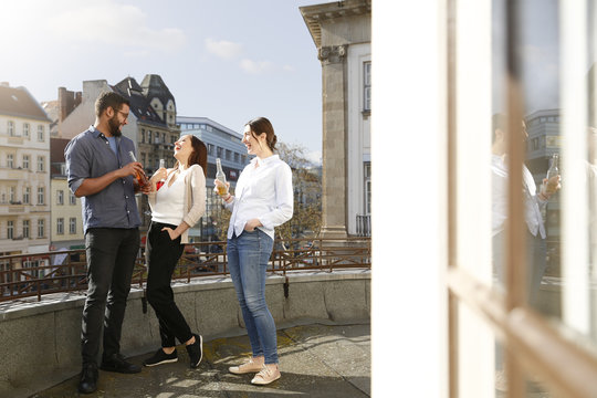 Happy man and two women with bottles on roof terrace