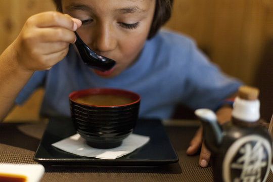 Little boy sitting in an Asian restaurant eating hot miso soup