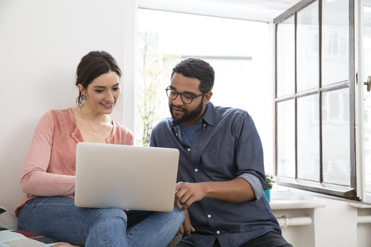 Man and woman sharing laptop at the window