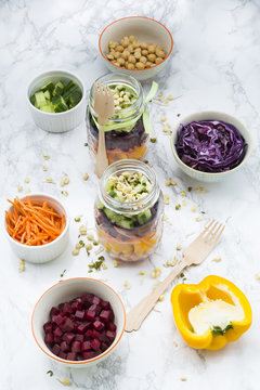 Two glasses of rainbow salad with chick-peas, sprouts and different vegetables and bowls with ingredients