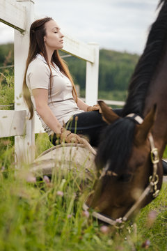 Young woman with brown horse having a break on paddock