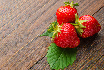 Three fresh strawberries with leaves on old wooden background