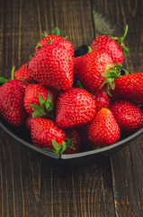Strawberries with leaves in black plate. wooden background.