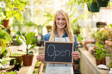Young woman holding open sign placard at greenhouse