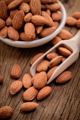 almonds in a white ceramic bowl on grained wood background
