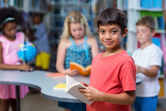 Smiling boy holding books against classmates