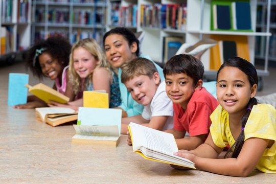 Happy teacher with children lying down while reading books
