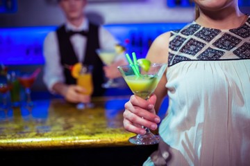 Woman with cocktail glass standing by bartender