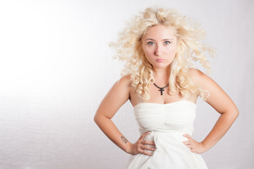 Fototapeta na wymiar Handsome young woman in white dress with curly hair looking seriosly with cross on her neck. Blonde girl with sensual lips and beautiful blue eyes.