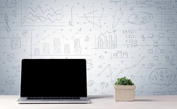 Laptop on desk with business charts on wall