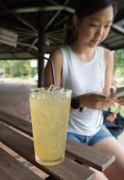 Glass of ice lemon tea and Asian woman scroll with her smartphone