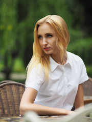 Obraz premium Beautiful young woman in white dress sitting at the cafe table a