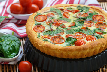 Summer outdoor tart, pie of fresh vegetables - tomatoes, spinach and red onion with cream and cheese. Selective focus
