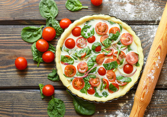 Baking a vegetables tart  with tomatoes and spinach. The ingredients on the table - dough, tomatoes, spinach, cream, eggs