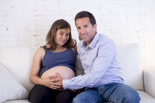 young couple in love at home living room couch with the woman being pregnant