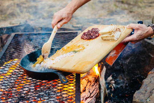 Person scraping ingredients from cutting board into frying pan on bbq