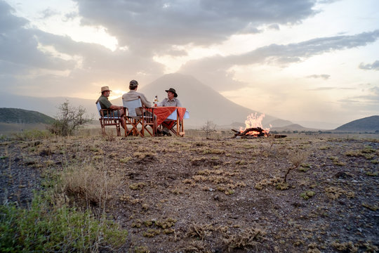 Men sitting at table by campfire sharing bottle of wine, Tanzania
