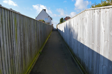 A path and wooden fences offers perspective as it leads towards a house in the background and cloudy blue skies. 