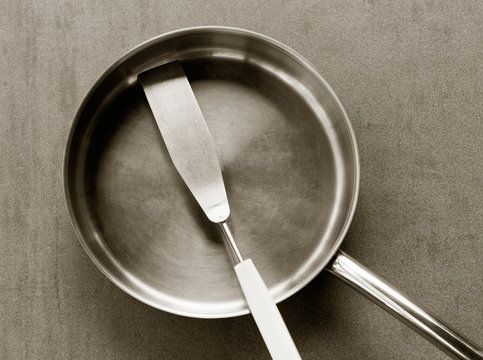 used clean empty stainless steel frying pan and spatula overhead view on the gray background, black white photos. closeup top view