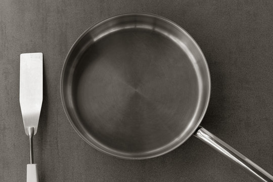 used clean empty stainless steel frying pan and spatula overhead view on the gray background, black white photos. closeup top view