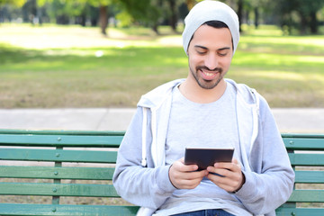 Young man using tablet sitting on park bench.