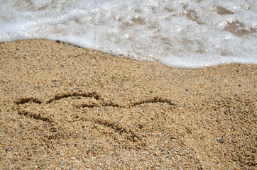 Two heart symbols written on beach sand with sea wave right behind it