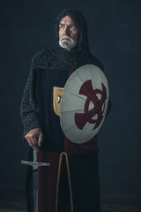 Knight with gray beard holding sword and shield.
