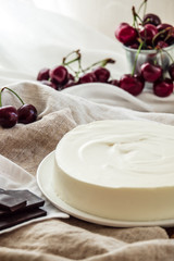 Light vanilla bavarian mousse cake with cream cheese and whipped cream. White plate. Ripe cherries and dark chocolate.