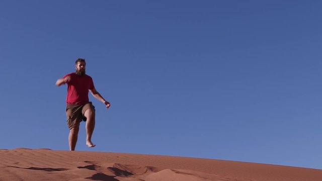 Slow motion of a man running and jumping down the face of a sand dune inside the Namib-Naukluft National Park 
