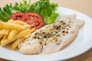 Grilled fish fillet steak with herb and french fries on plate