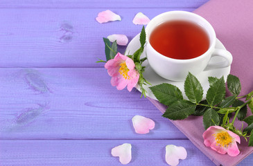 Cup of tea and wild rose flower on purple boards, copy space for text