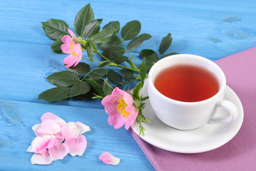 Fototapeta na wymiar Cup of tea and wild rose flower on blue boards