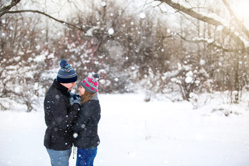 Fototapeta na wymiar Loving couple embracing in winter park. Loving warm hands to each other. Copy space. The girl hat with red hearts