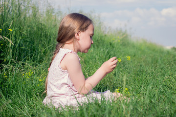 Little Girl Sitting In Meadow Field Picking Flowers 