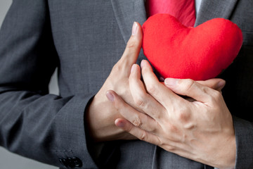Businessman showing compassion holding red heart onto his chest
