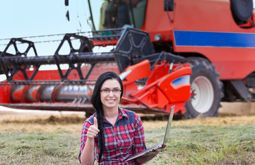 Farmer girl with laptop and combine harvester