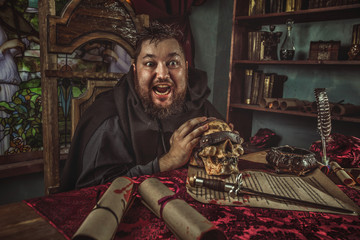 Smiling medieval fat monk in sitting in the dark room.