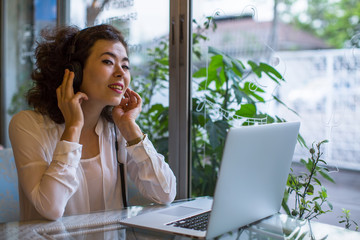 Obraz premium Asian girl sitting at a table in a cafe with a laptop, in headphones to enjoy music.