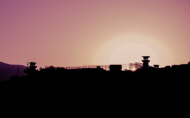 Silhouette of barbed wires and watchtower of prison in Neapolis, Crete, at sunset 