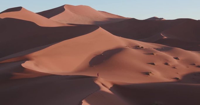 4K panning shot of male tourist admiring the view of endless sand dunes of the Namib desert inside the Namib-Naukluft National Park 