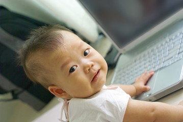 Asian infant is smiling on the floor with laptop computer.